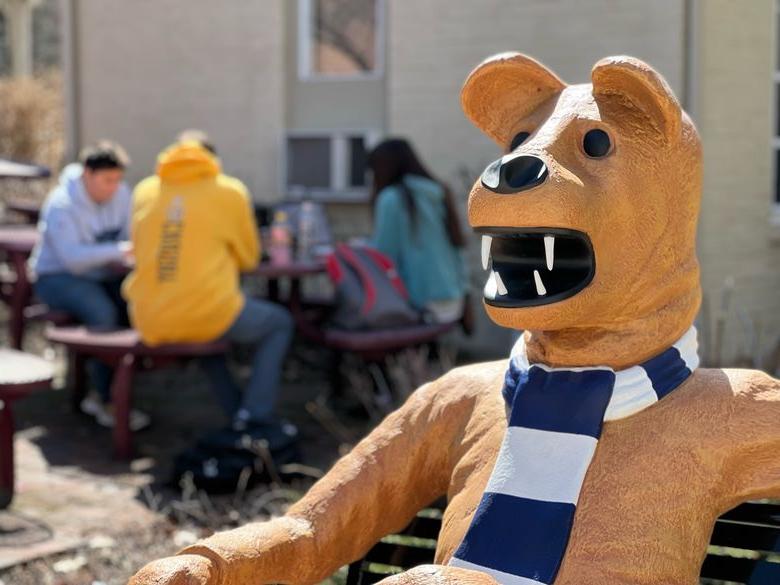 Students socialize behind the Nittany Lion mascot on a bench